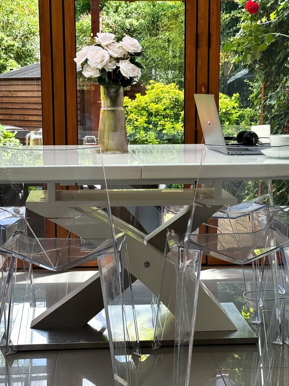 A glass dining table set with white roses, looking out onto a garden