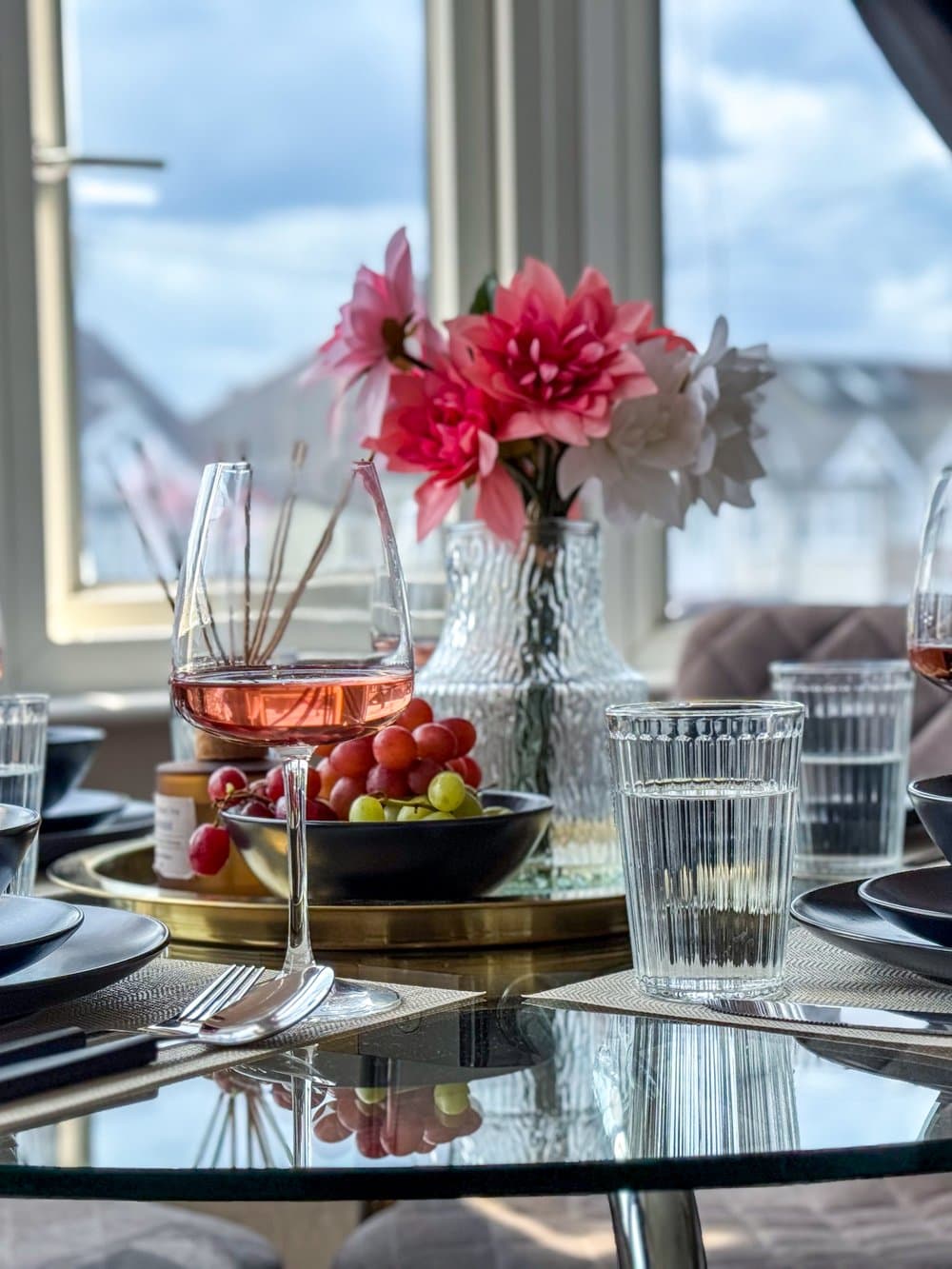 A dining table laid with wine and fruit by a bright bay window